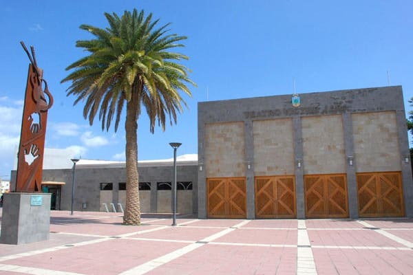 Fachada del Teatro Víctor Jara en Vecindario, con la escultura homenaje a Víctor Jara y la palmera junto a la plaza de acceso